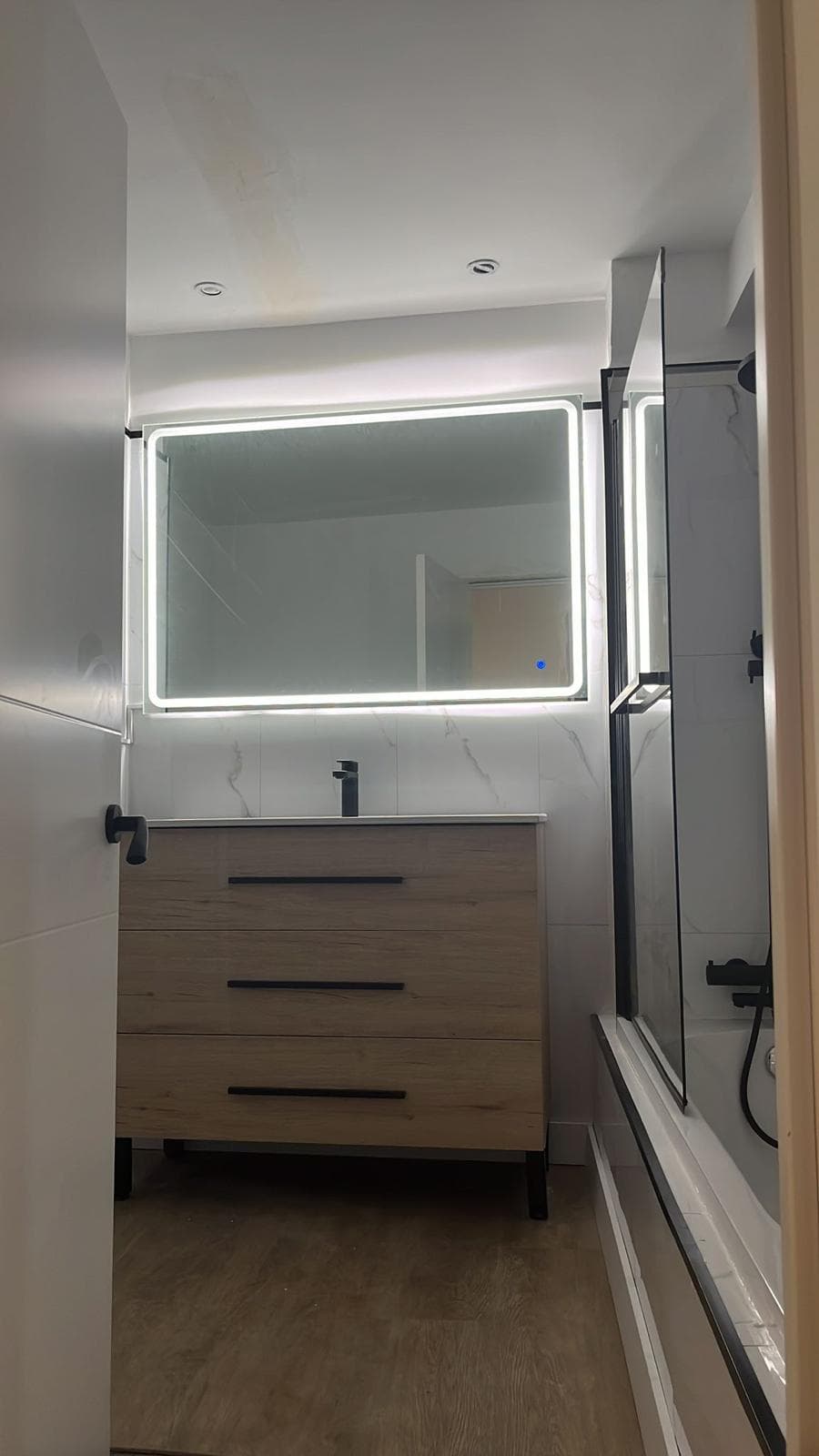 Baño reformado con mueble de lavabo de madera, espejo con luz led y mampara negra