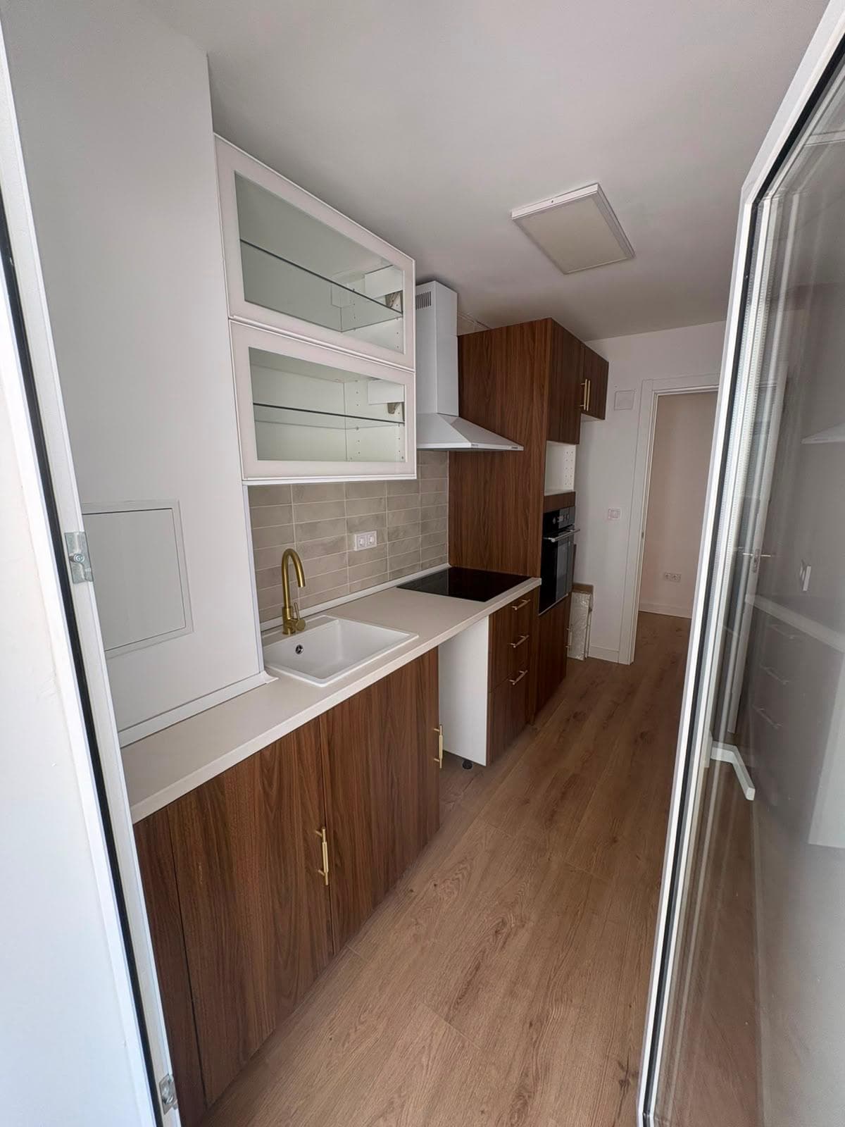 Cocina reformada con muebles de madera, encimera blanca y suelo laminado